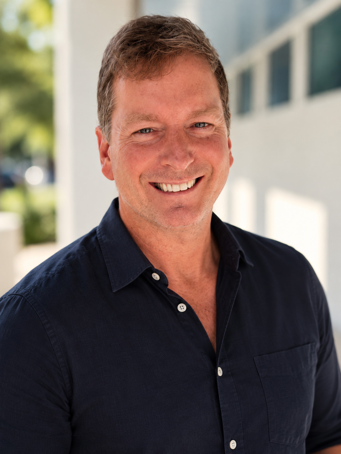 A man with short blonde hair and a navy shirt smiles at the camera'