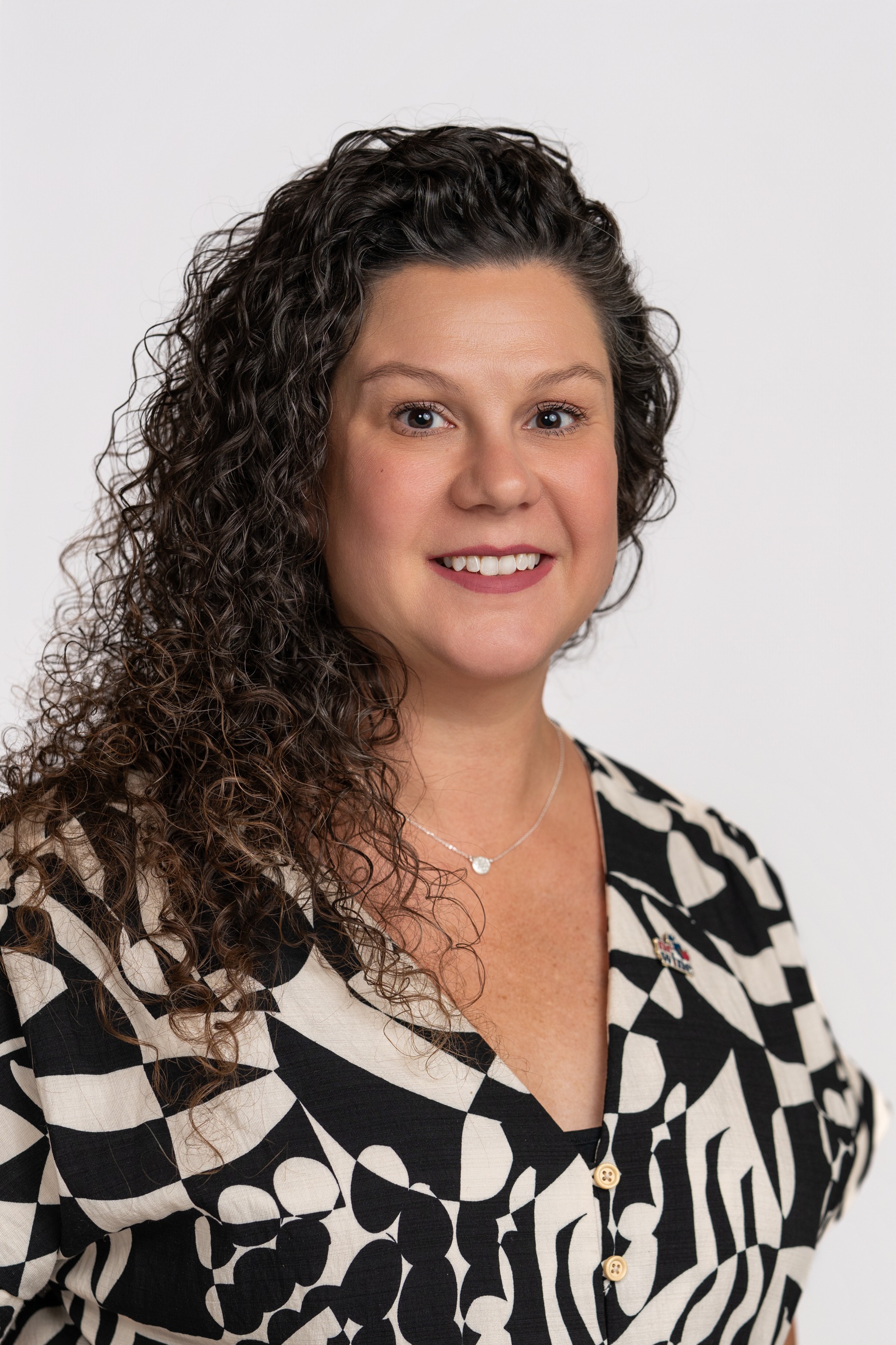 A woman with black curly hair and a black and white pattern top smiles at the camera