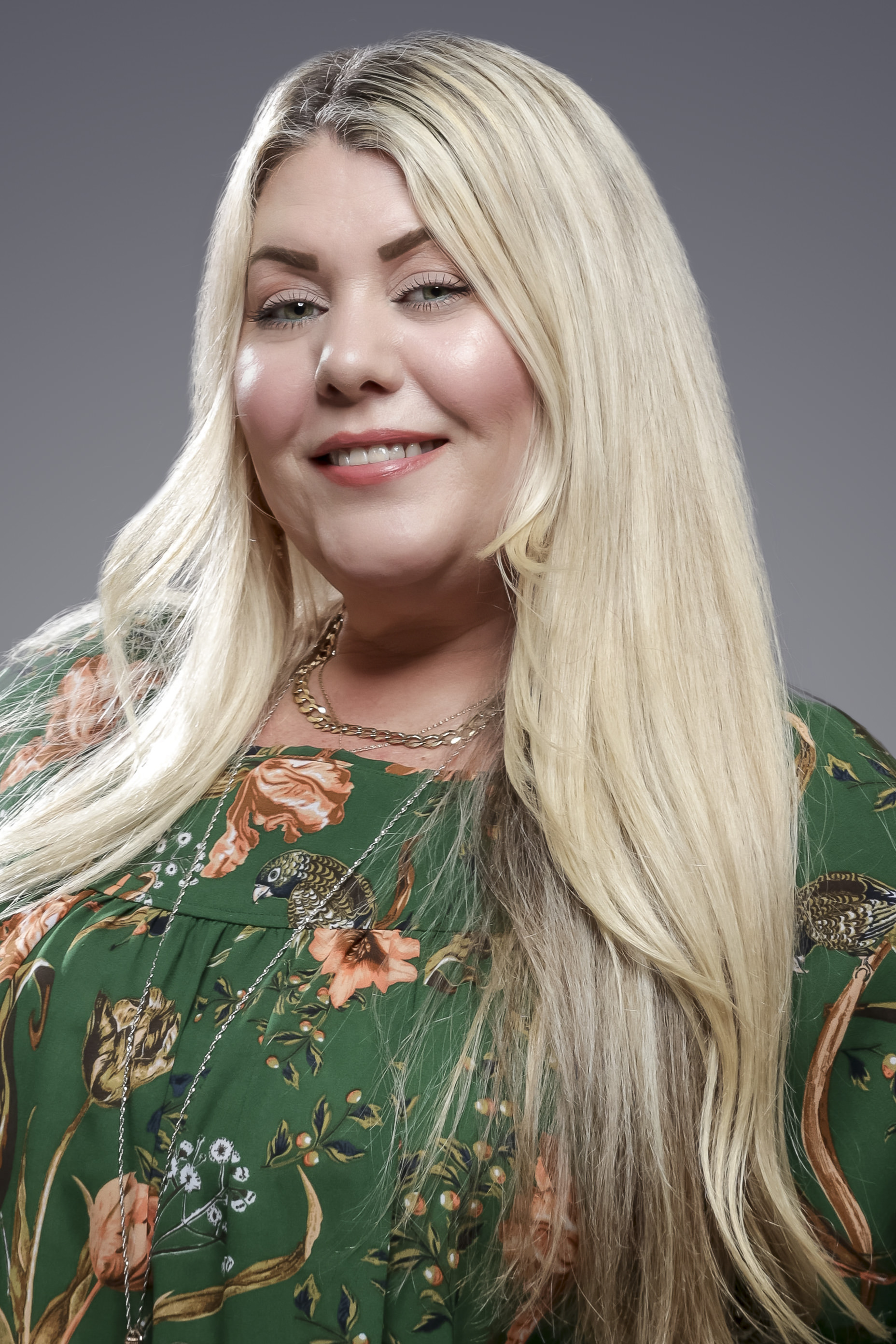 A blonde woman in a green floral shirt smiles at the camera.