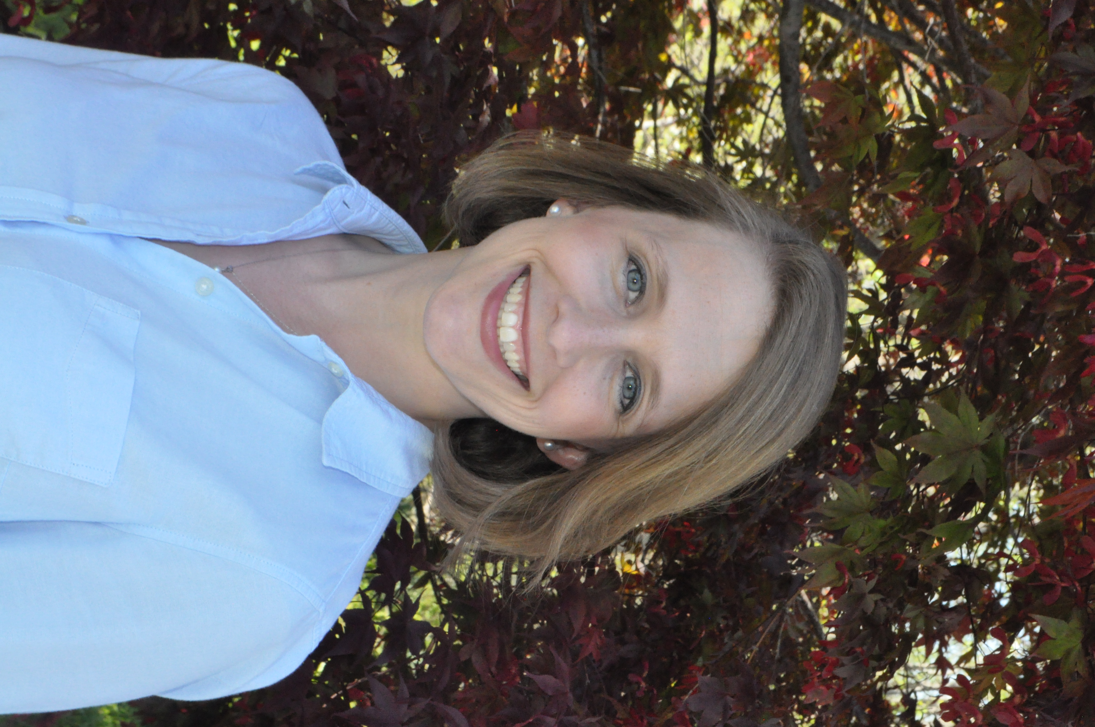 A woman with blonde hair and a light blue shirt smiles at the camera