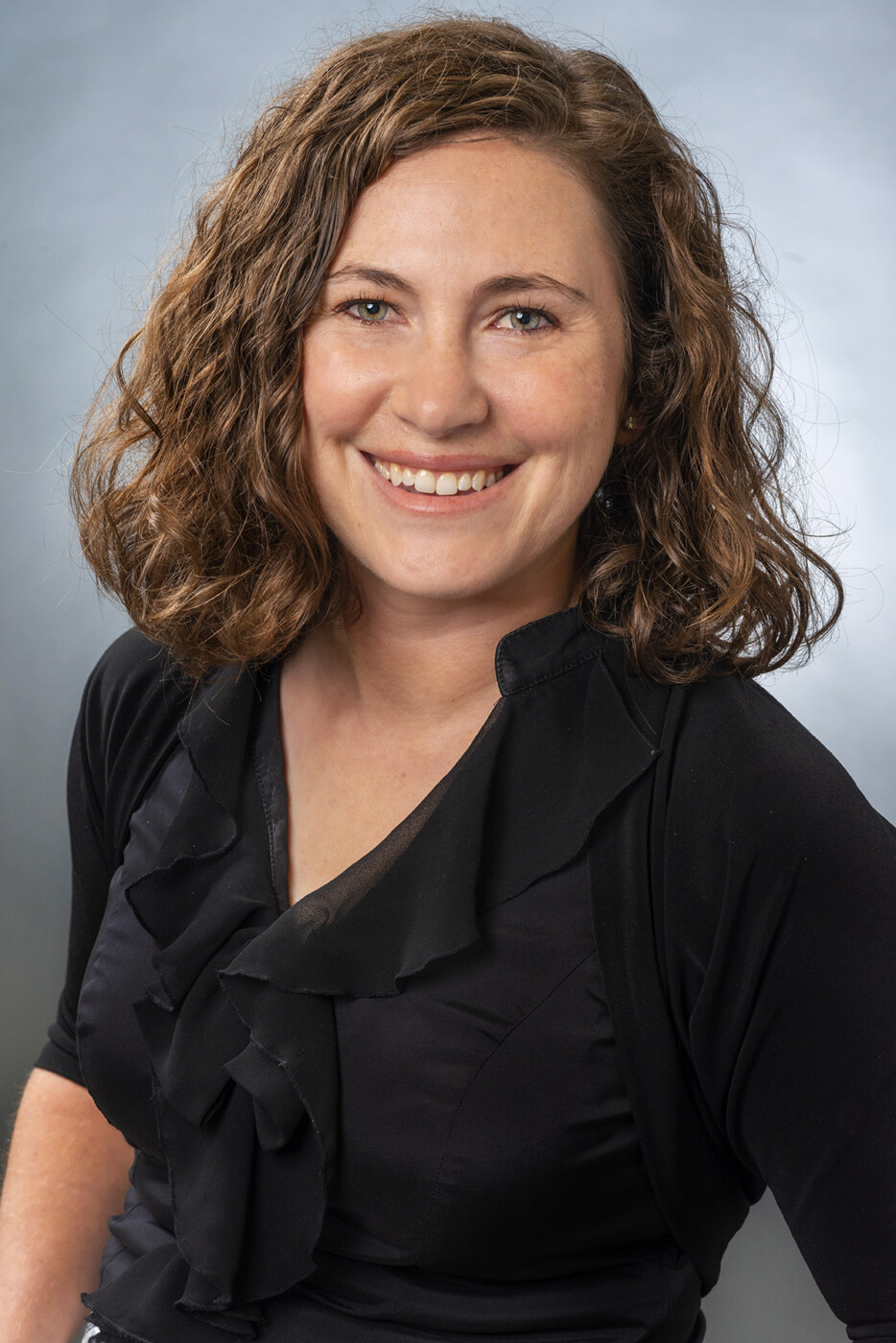 A woman with short brown hair and a black shirt smiles at the camera