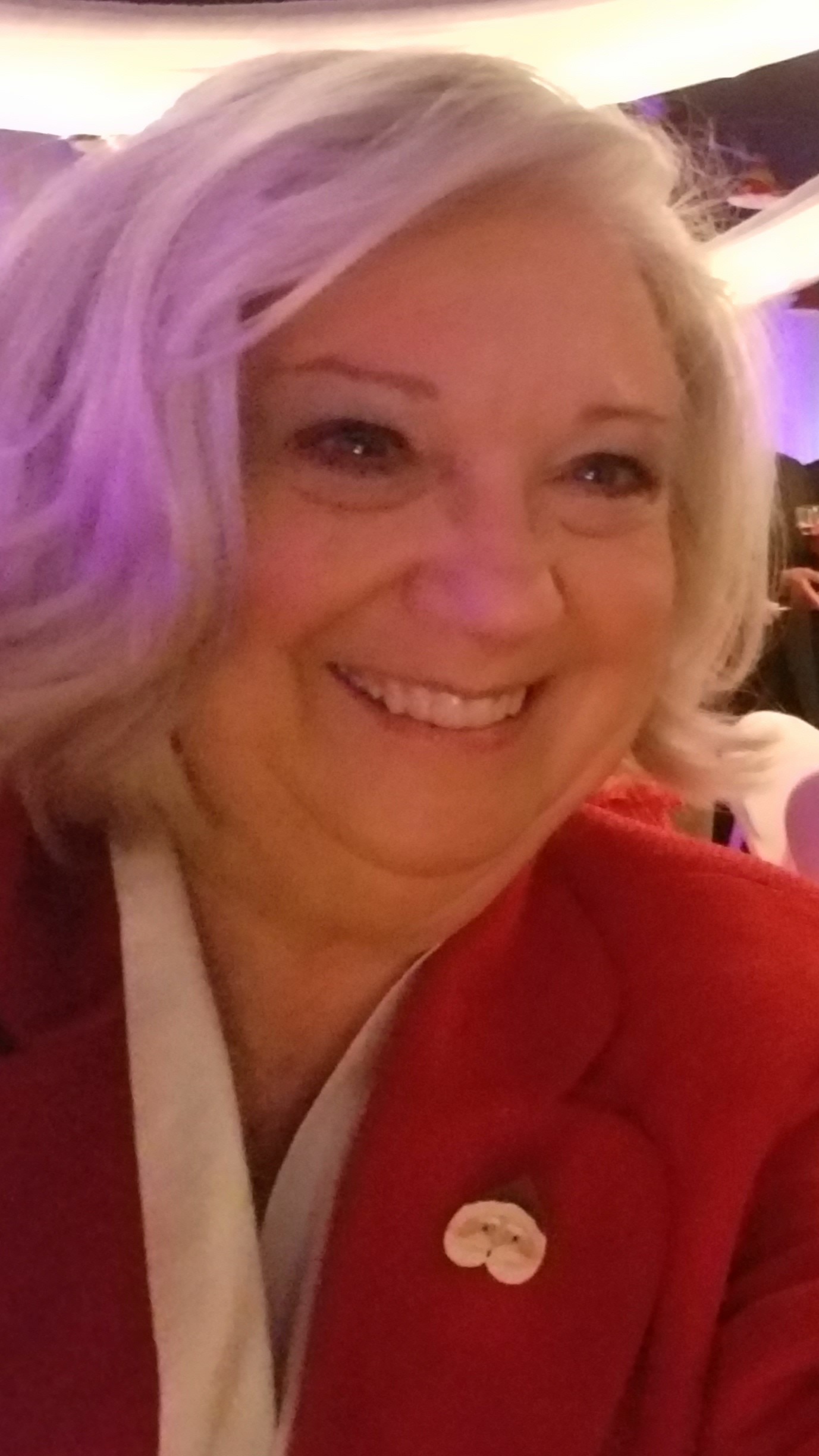 A woman with white hair and a red shirt smiles at the camera