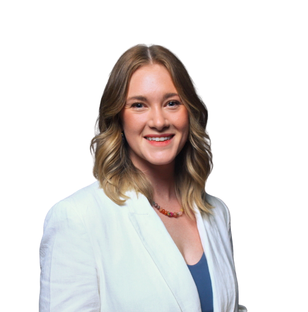 A blonde woman wearing a light blue blazer with a dark blue shirt underneath stands smiling at the camera