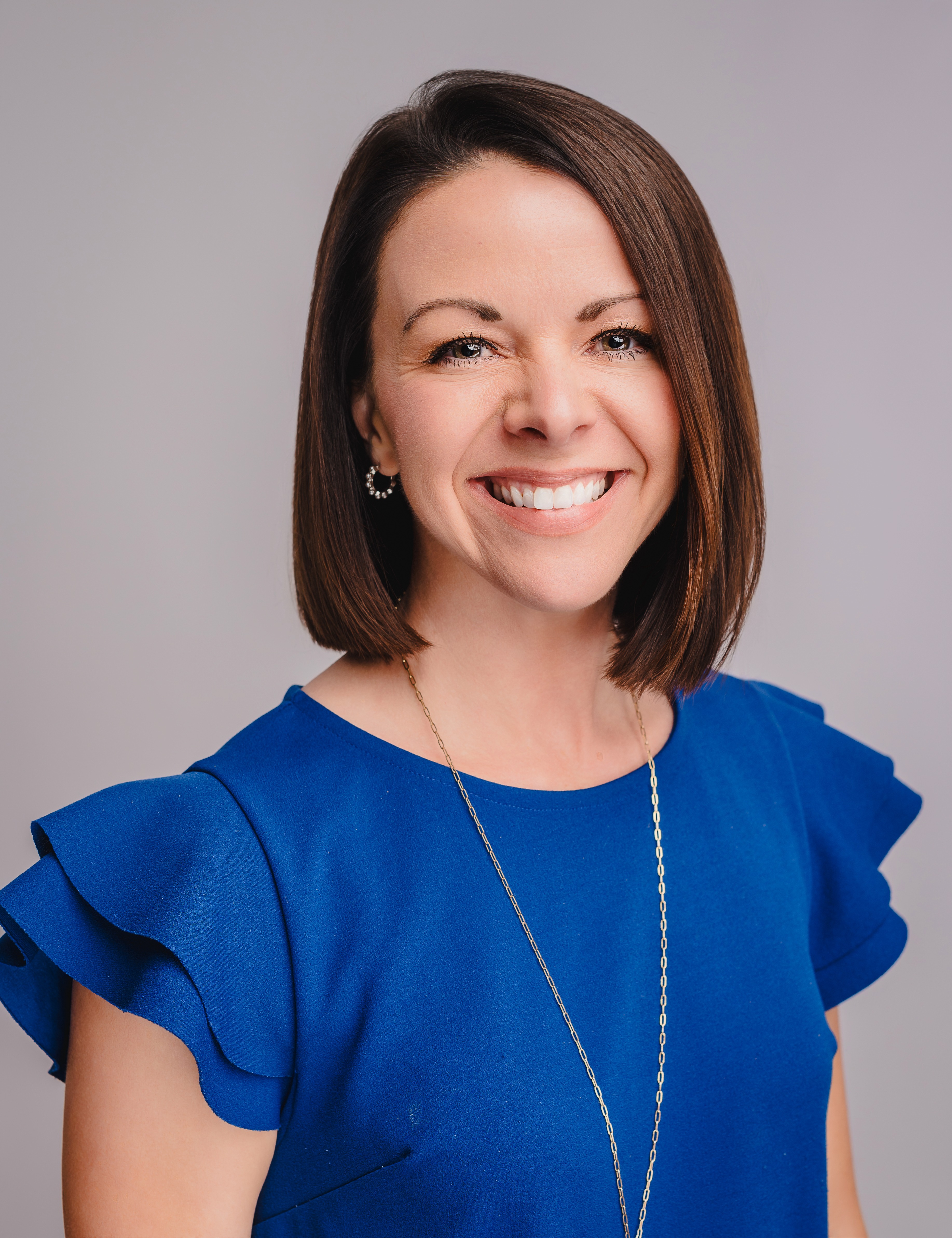 A woman with short brown hair and a royal blue shirt smiles at the camera