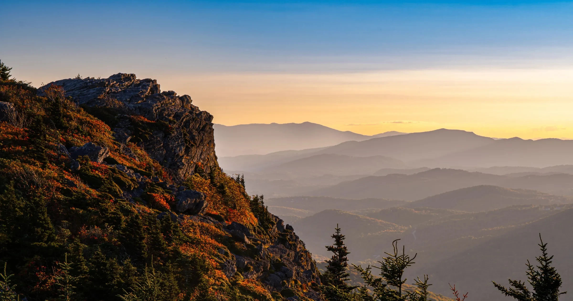 View of the side of Linville Peak with a colorful, hazy view of adjacent peaks. 