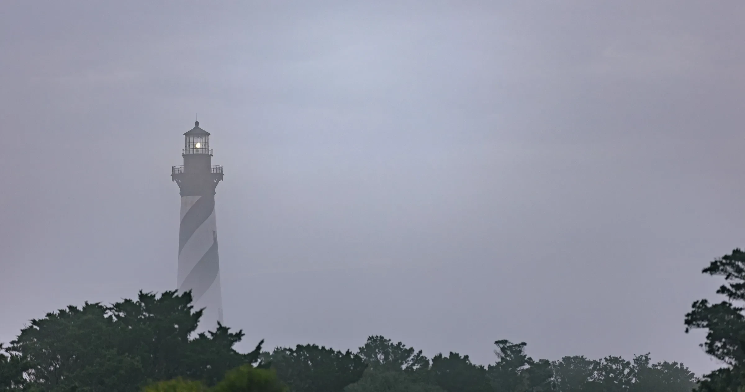 Cape Hatteras lighthouse rises out of the fog above the trees.