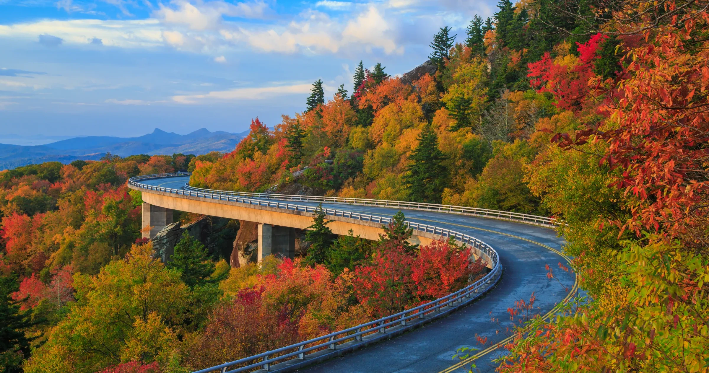 Linn Cove Viaduct section of Blue Ridge Parkway meandering around mountain surrounded by fall foliage.