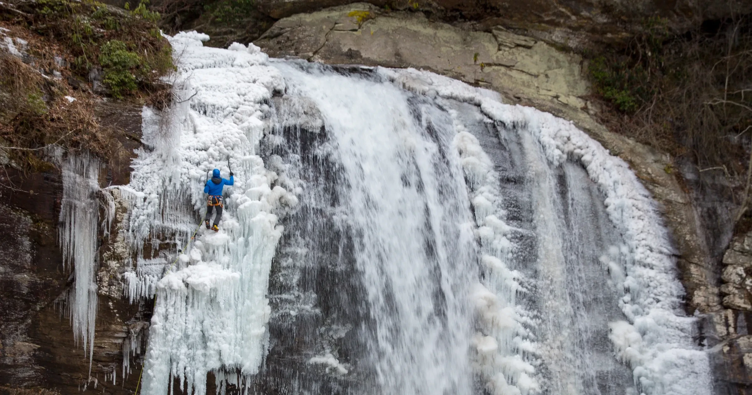 Man ice climbing up waterfall in winter in Brevard area.