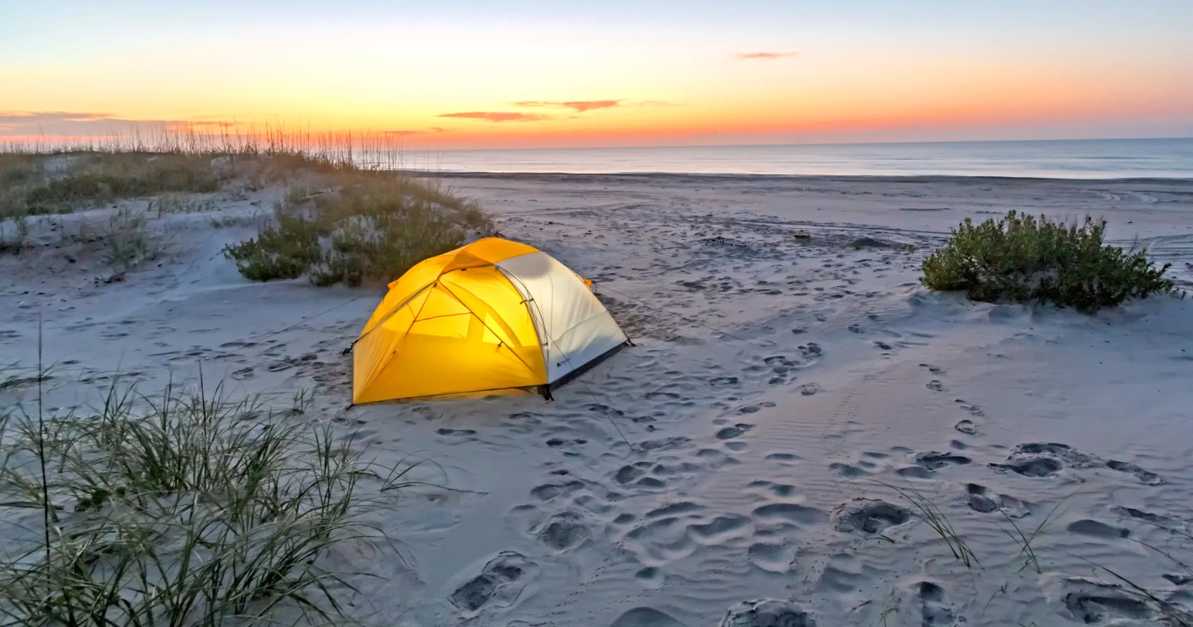 Yellow tent is aglow with light along Cape Lookout National Seashore with sunrise in the distance.