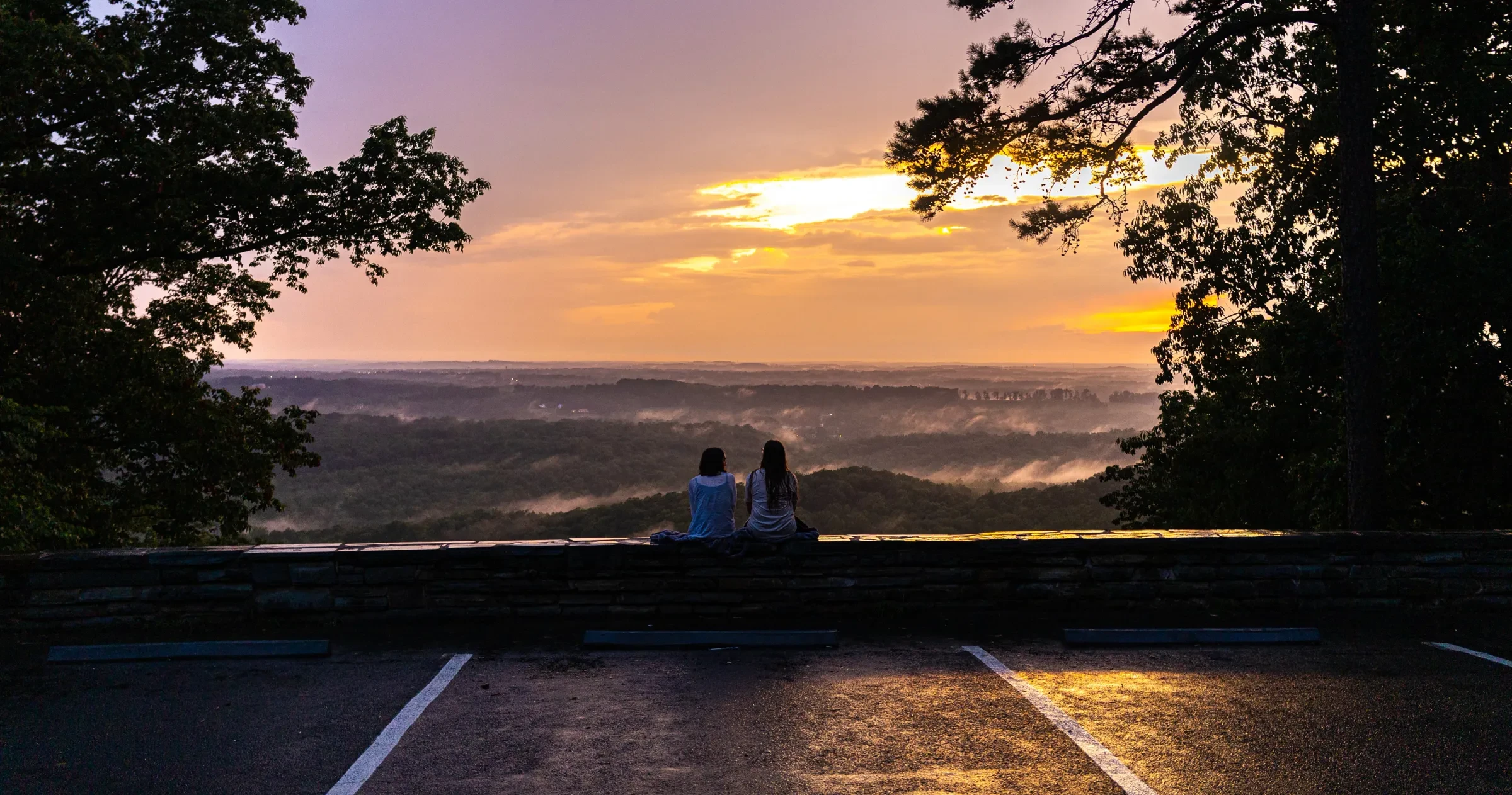 Backs of two friends sitting on ledge during sunset at Morrow Mountain State Park.