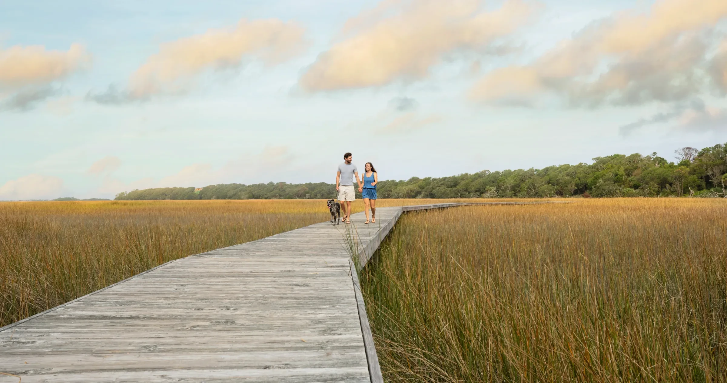 Couple walking dog on wooden walkway through marsh on Bald Head Island.