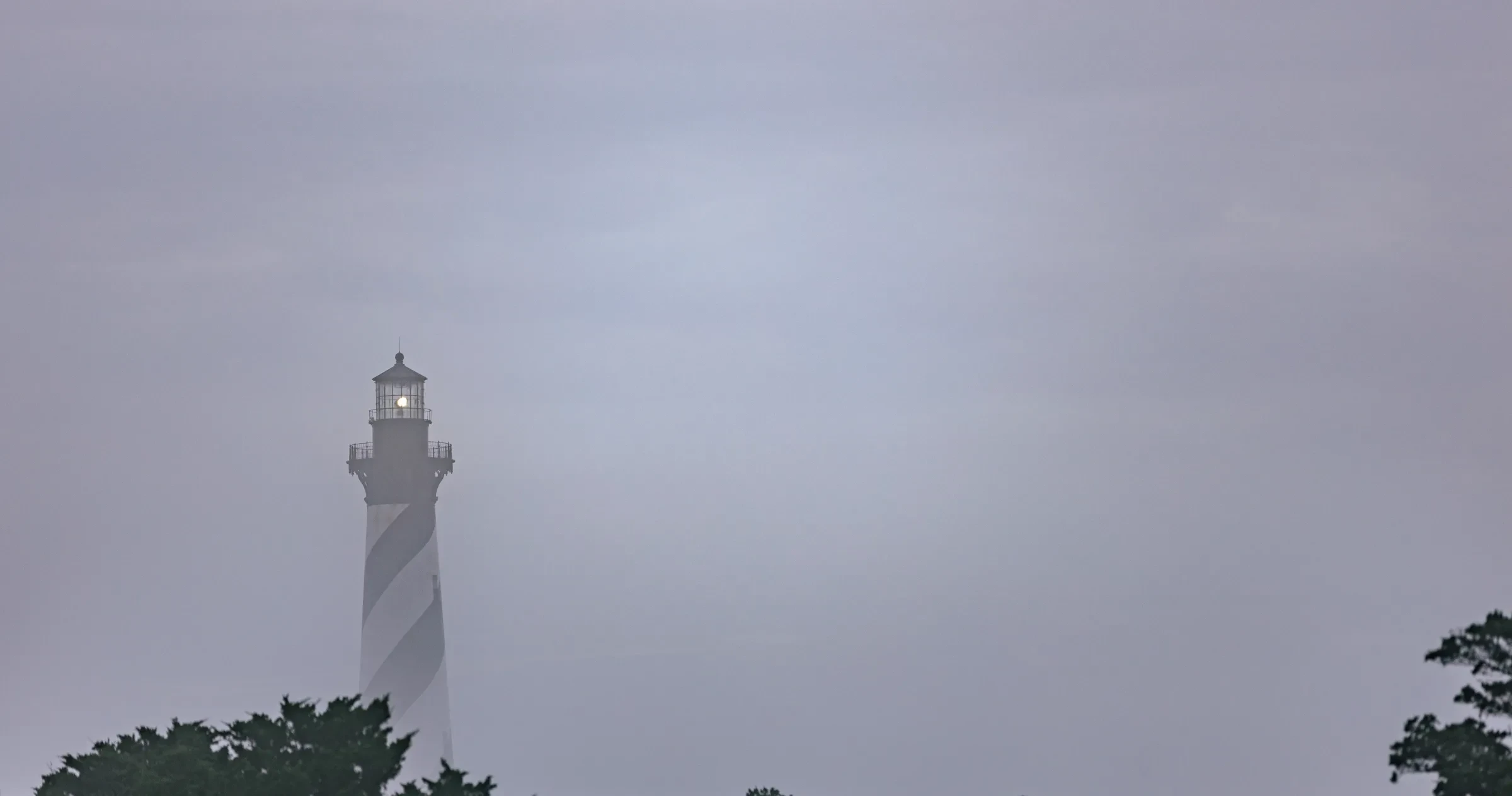 Cape Hatteras lighthouse rises out of the fog above the trees.