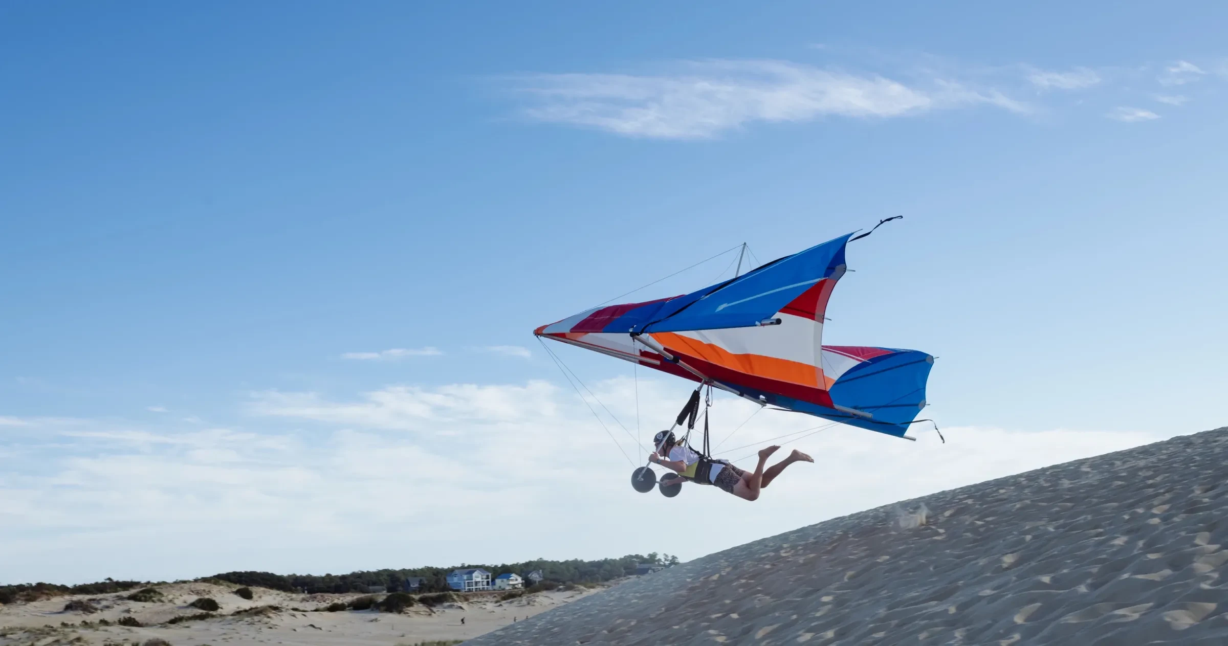 Person hang gliding over sand dunes during daytime.