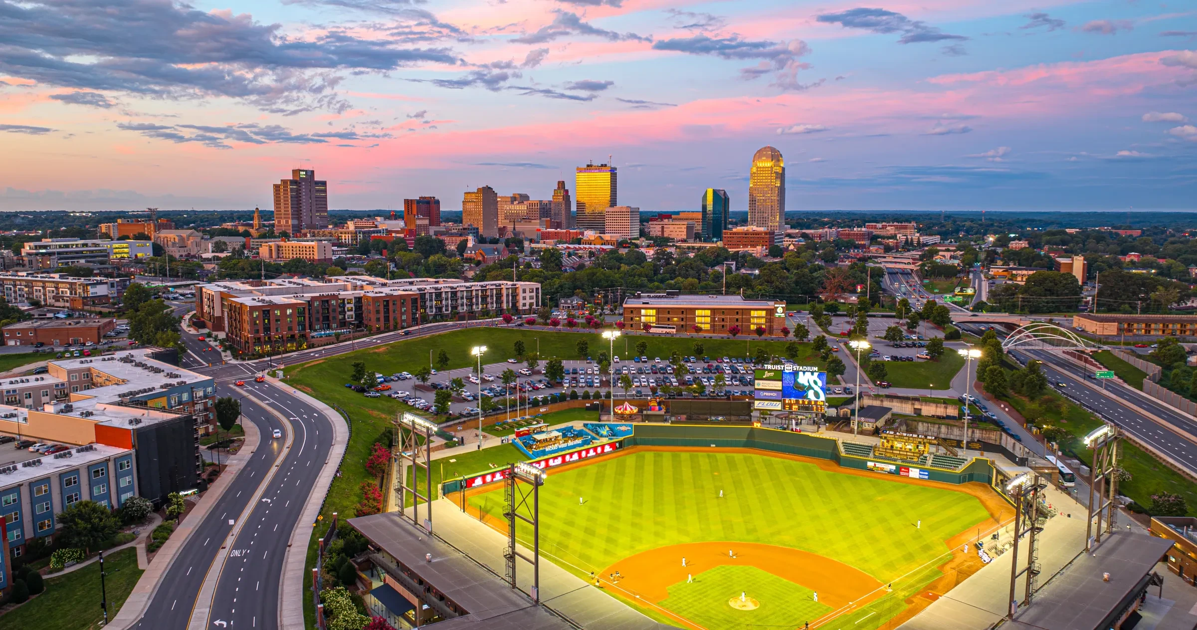 Aerial of Winston-Salem's Truist Stadium baseball park with skyline in background at dusk.
