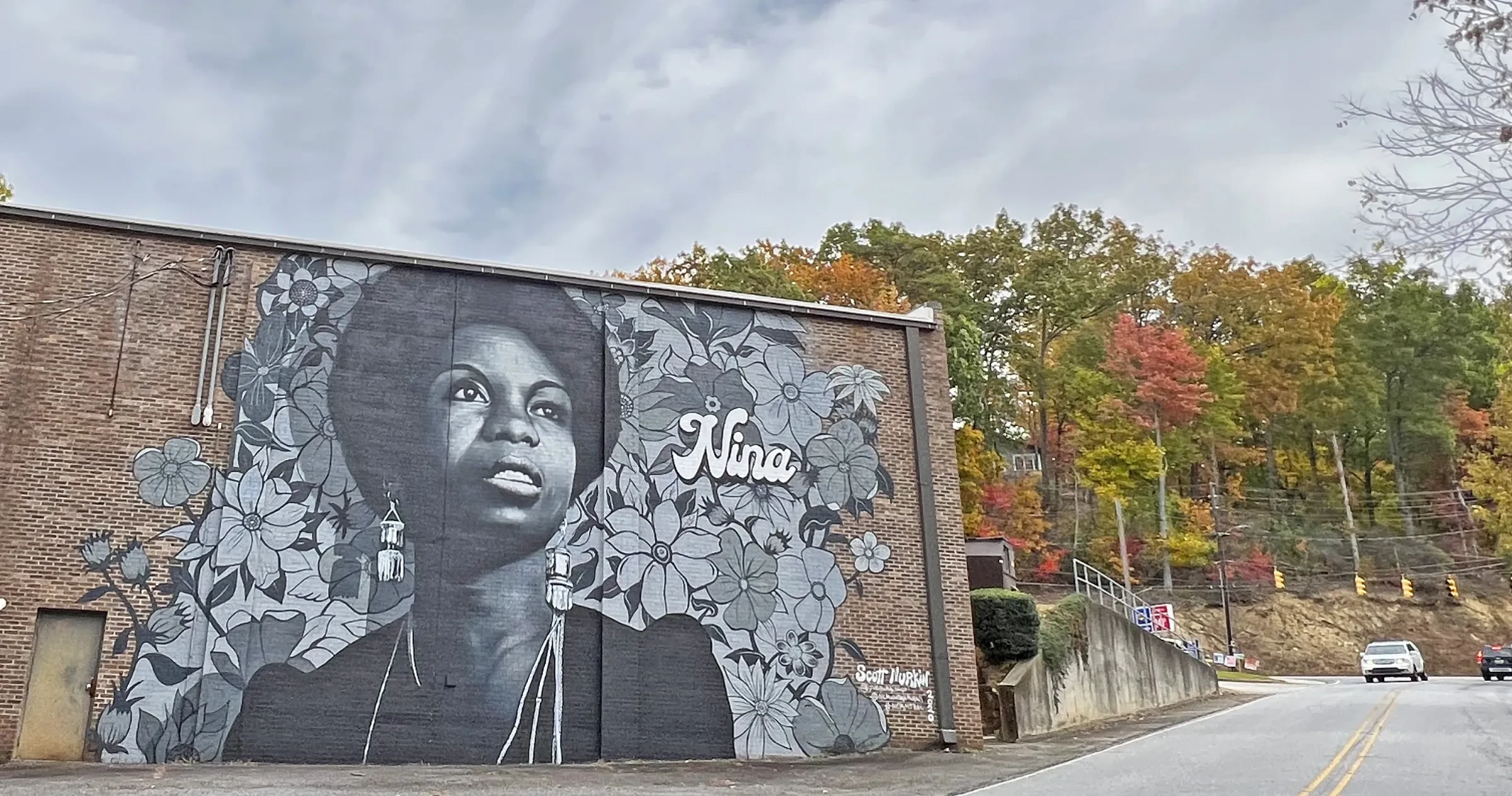 Nina Simone mural on the side of brick building beside road.