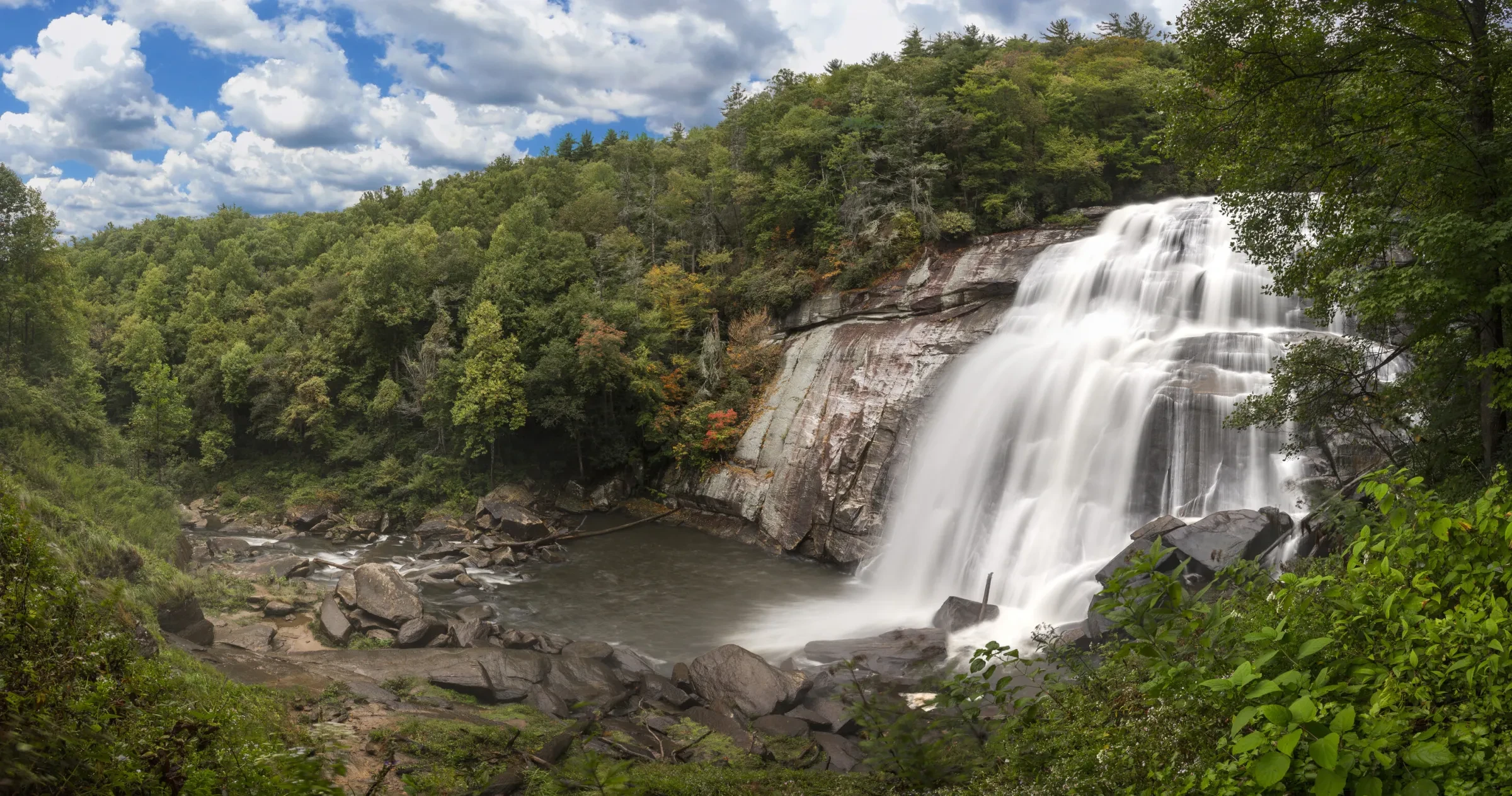 Waterfall cascading into large pool of water surrounded by green trees.