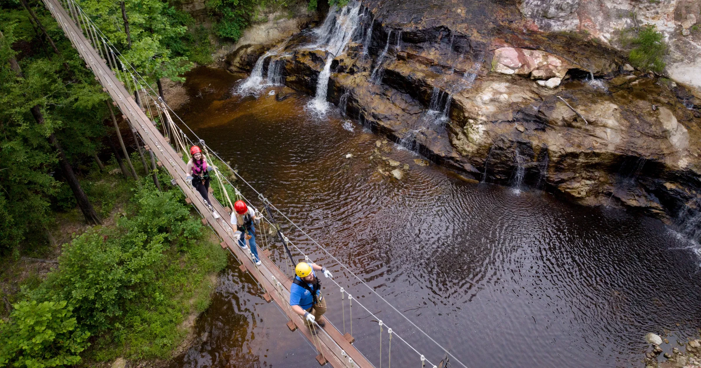People walking on drawbridge over waterfalls and creek.