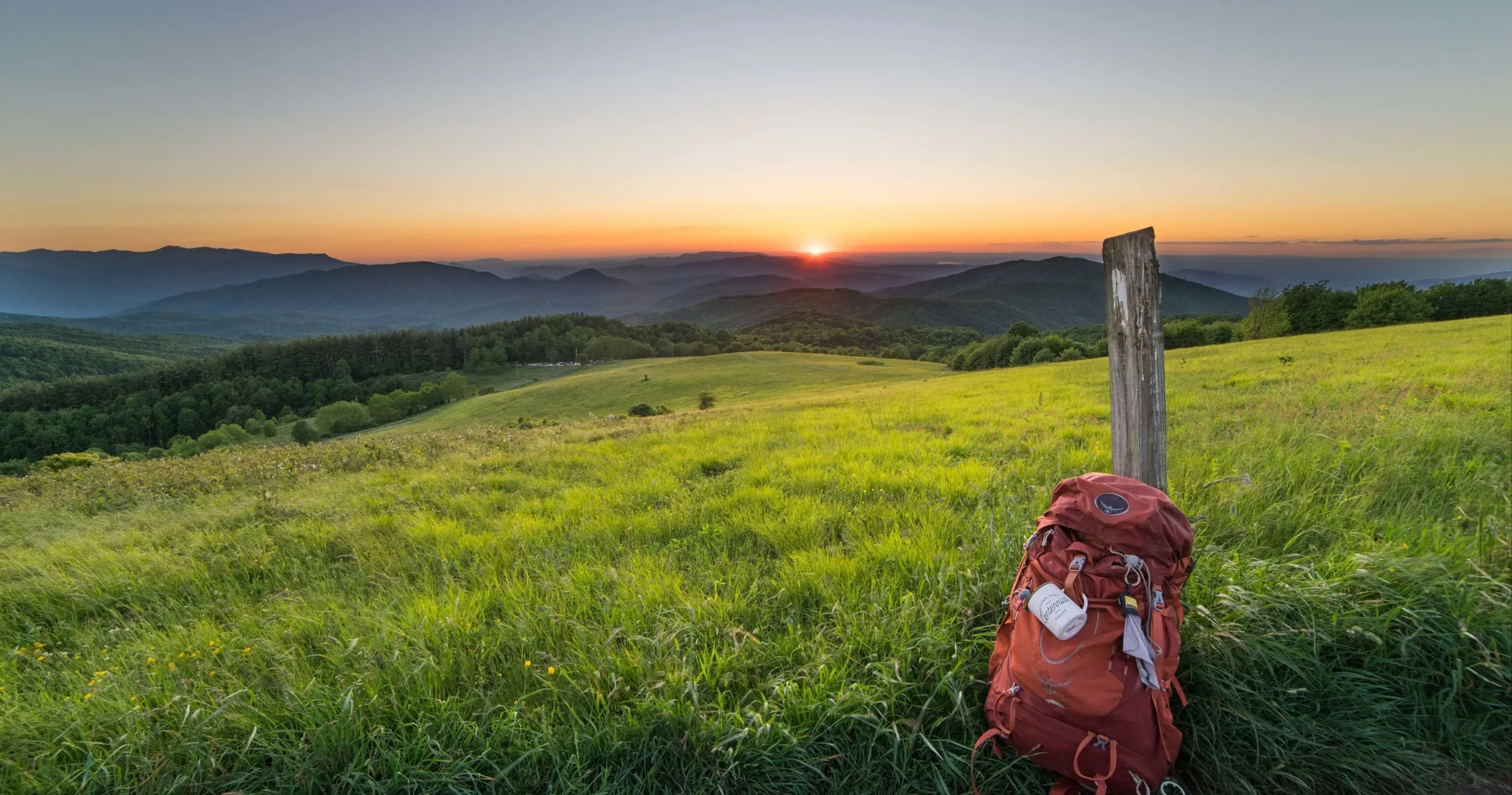 Backpack sitting against wooden post with sun rising over Appalachian Mountains at sunrise.