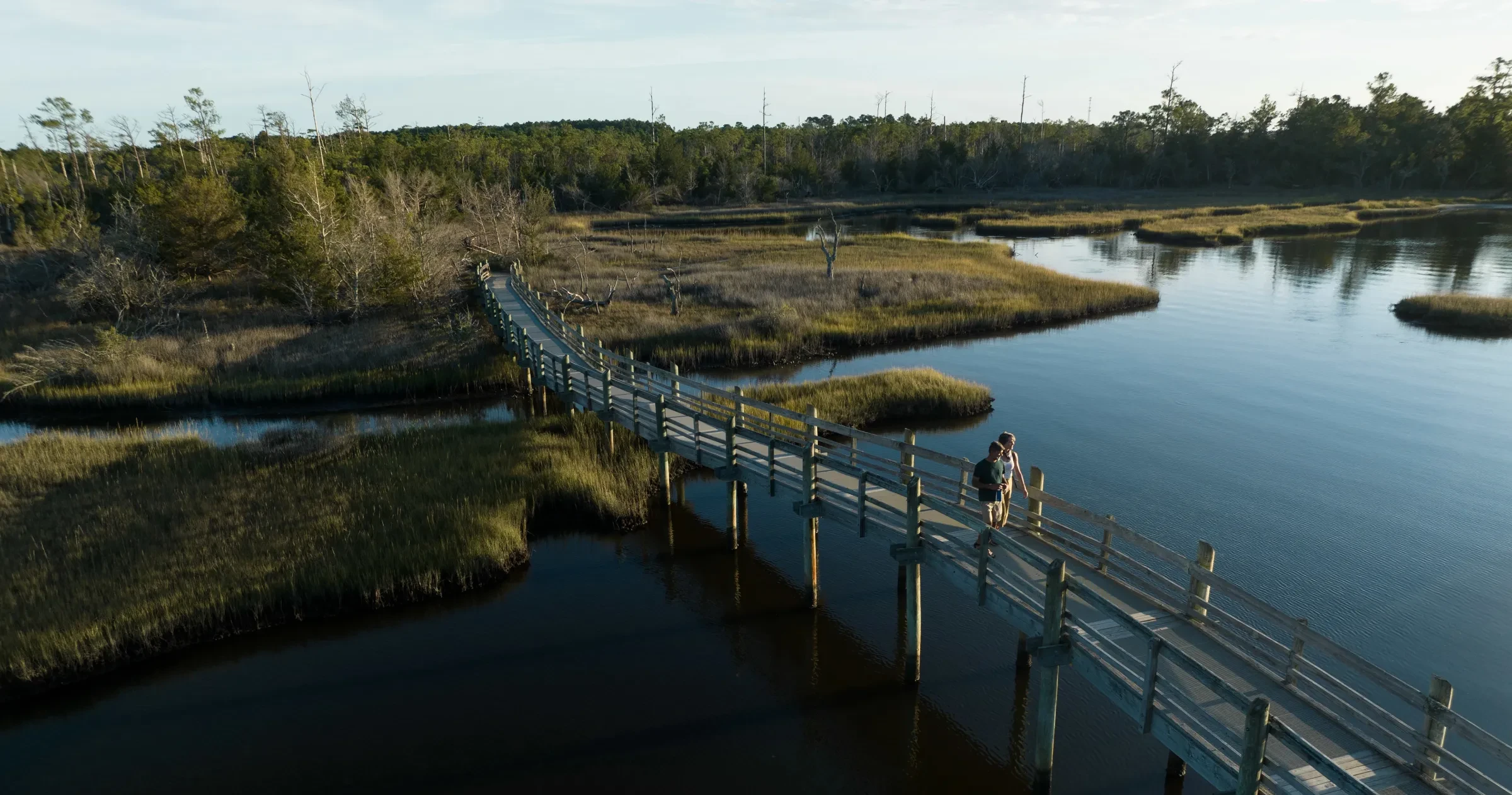 Aerial of two people walking on bridge over marsh in coastal forest