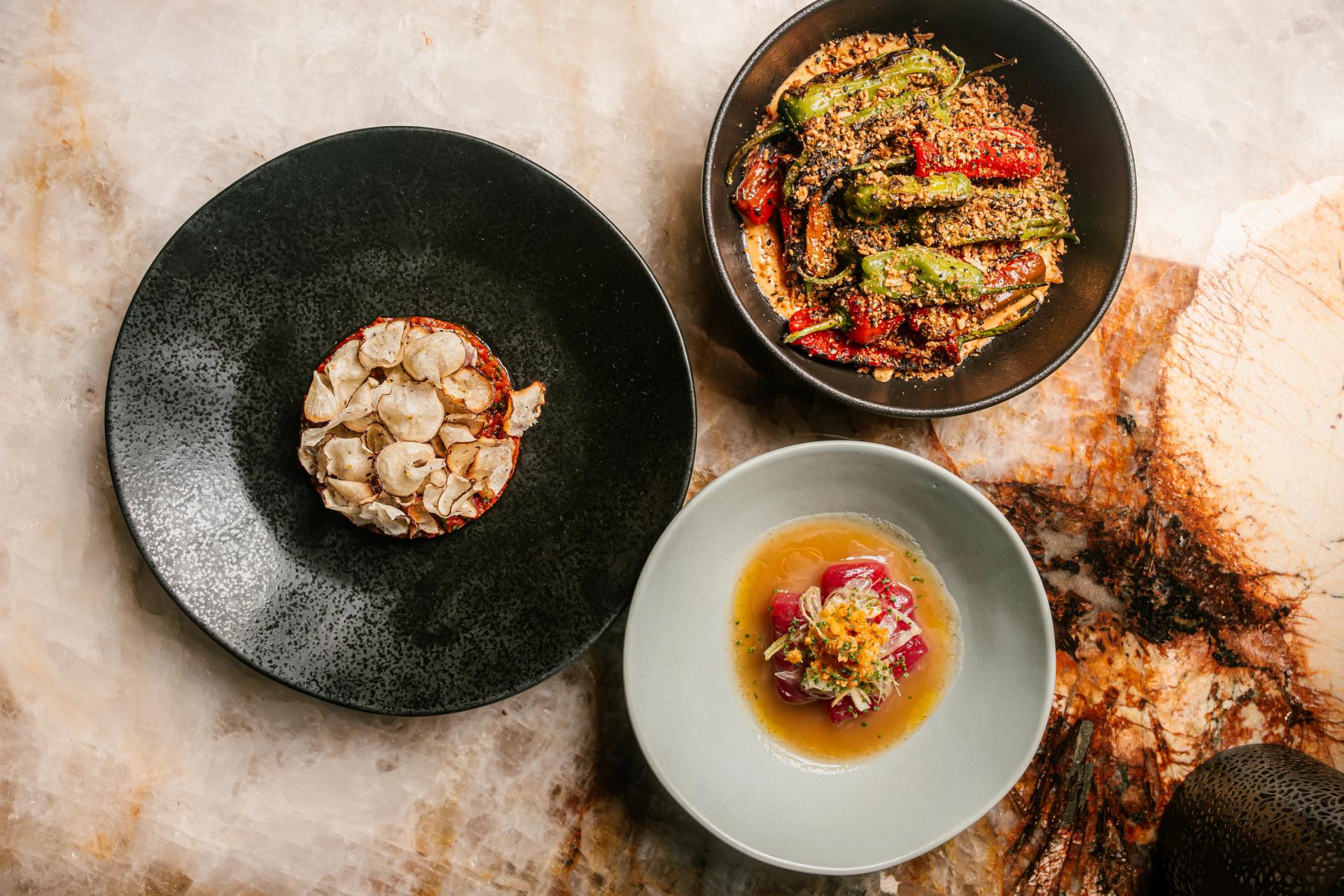 Overhead of three beautifully plated dishes sitting on marble table at Customshop.