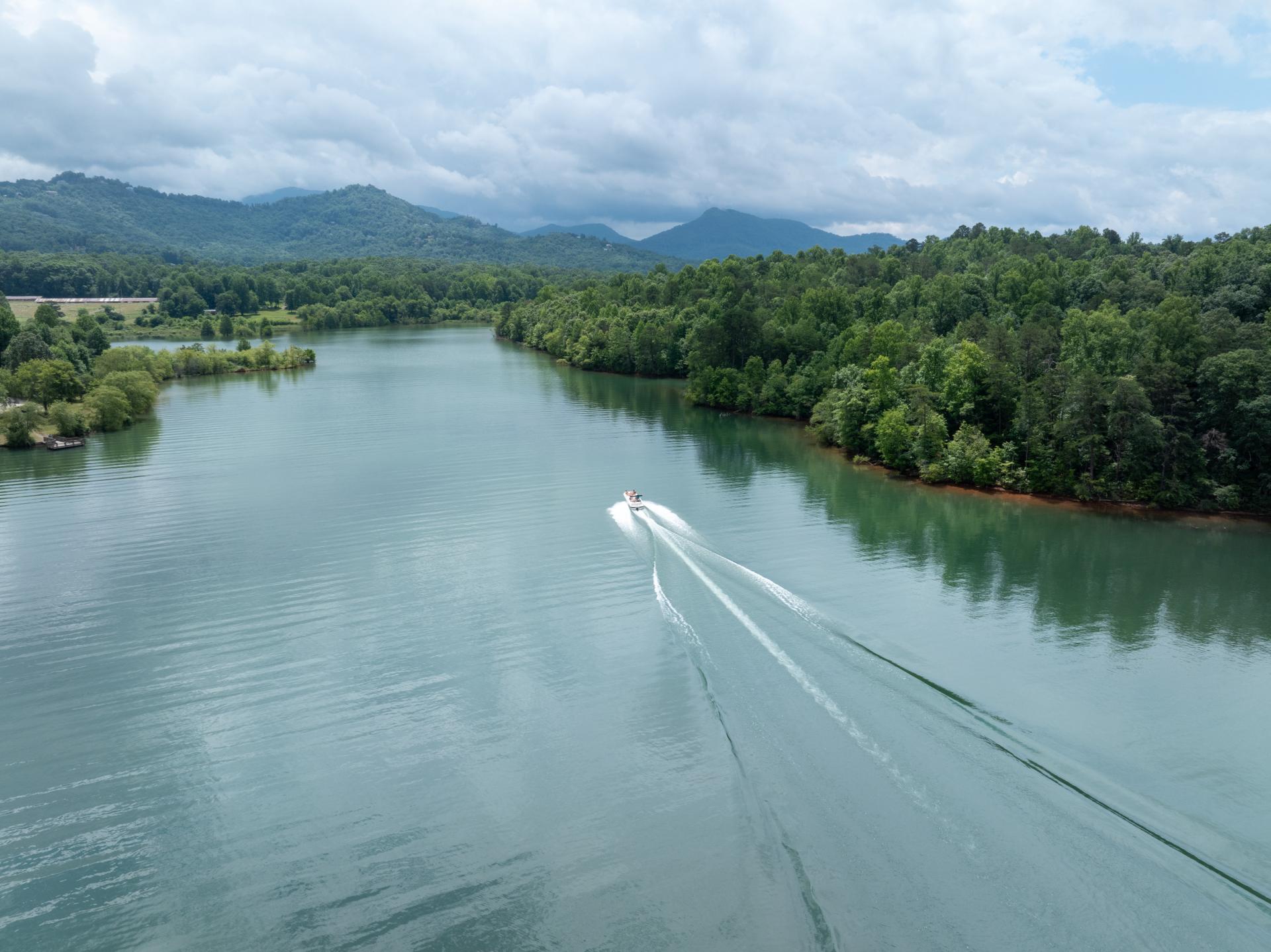 Aerial of boat wading through Lake Chatuge surrounded by trees and mountains in summer.