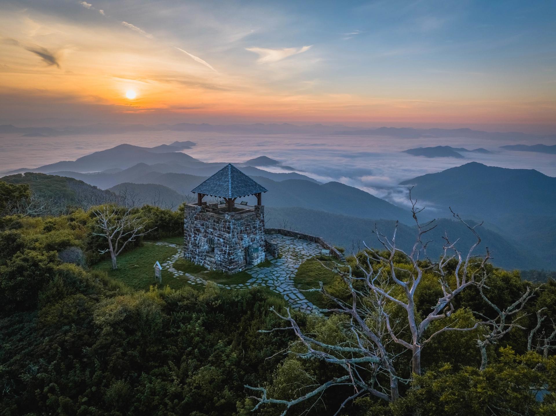 Aerial of Wayah Bald Tower made of stone sitting among trees looking out onto vast mountain vistas during fall.