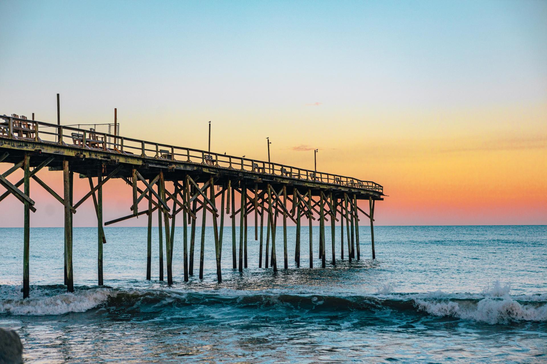 Wooden pier jutting out into ocean with beautiful orange and pink sky over ocean in distance