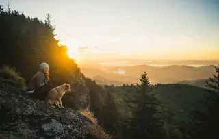 Woman sitting on cliff ledge with Dog in Mountains