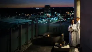 Couple in robes relaxing next to water tub on balcony