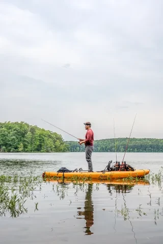 A man standing in kayak fishing on Badin Lake in Uwharrie National Forest, North Carolina. The calm waters of the lake reflect the soft, golden light of dawn, enhancing the peaceful solitude of the moment.