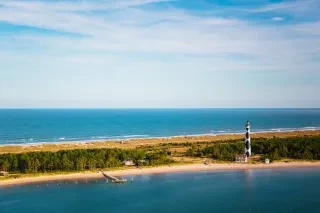 Distant aerial view of Cape Lookout National Seashore with Cape Lookout lighthouse and Keeper’s Quarters Museum and gift shop to the far right, dock to the far left. 