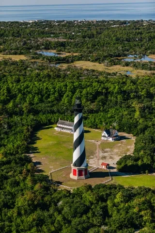 Aerial of Cape Hatteras Lighthouse and grounds with Keepers Quarters, surrounded by Buxton Woods, a martime forest, and Buxton Village in background.