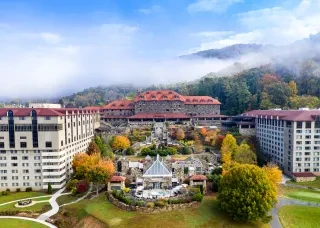 Aerial of full Omni Grove Park Inn buildings and grounds, full of fall foliage with mountains in background.