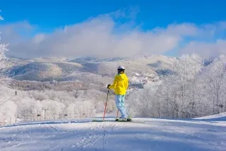 Skiier at top of Sugar Mountain Resort slope taking in snowy mountains in background.