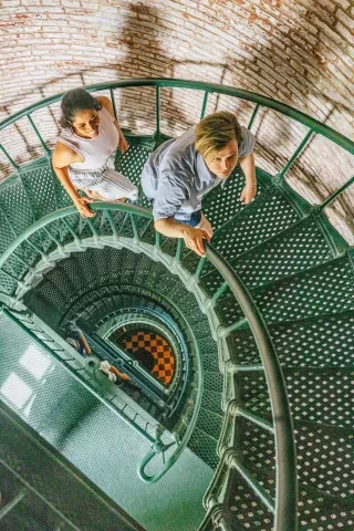 Couple climbing up spiral staircase within Currituck Beach Lighthouse. 