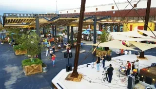 Landscape aerial view of Camp North End outdoor picnic and concert area at dusk. People mingling in background with stage in lower right corner in foreground.