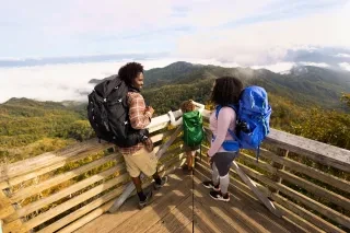 A family in the middle of frame fitted with backpacking gear with clouds falling on summits with horizon in background at Wesser Bald Fire Tower in Franklin, NC.