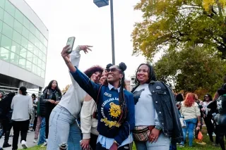 Group of four friends taking a selfie and wearing NC A&T gear with other students in background.