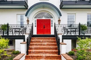 Exterior of white mansion inn with bright red door and brick steps leading to landing.
