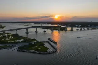 A breathtaking sunset view over the Surf City Bridge, with golden hues reflecting on the water. The setting captures the charm and serenity of the area during dusk.