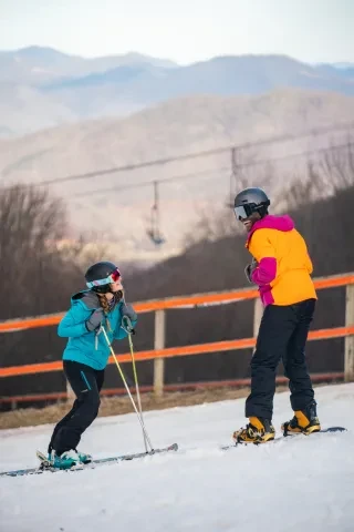 Couple smiling at each other on ski slopes at Cataloochee Ski Area with mountains in background.