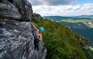 Woman rockclimbing in Linville Gorge with vast beautiful wilderness in background.
