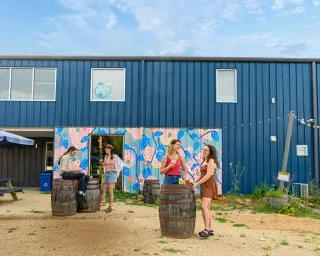 Friends enjoying beers outside by barrels at farm brewery in Mebane.