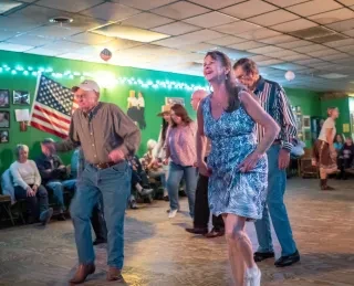 People line dancing in middle of dance floor with observers sitting along wall.