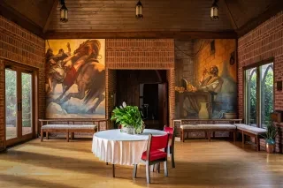 Ben Long frescoes on display on walls at St. Pauls with white tablecloth table and chair in front of it.