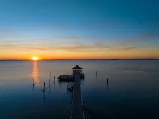 Pier jutting out into calm water during sunrise in Corolla.