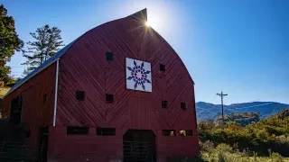 Sun shining on top of red barn with Quilt Block on its front.