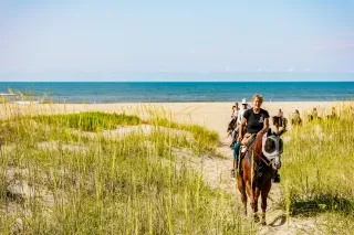 Person on horse leading tour through Hatteras Island dunes and beaches.