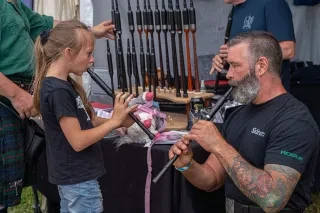 Man teaching girl how to play instrument at Grandfather Mountain Highland Games.