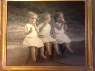 Framed photo of triplet siblings eating ice cream while sitting on a ledge at a park.